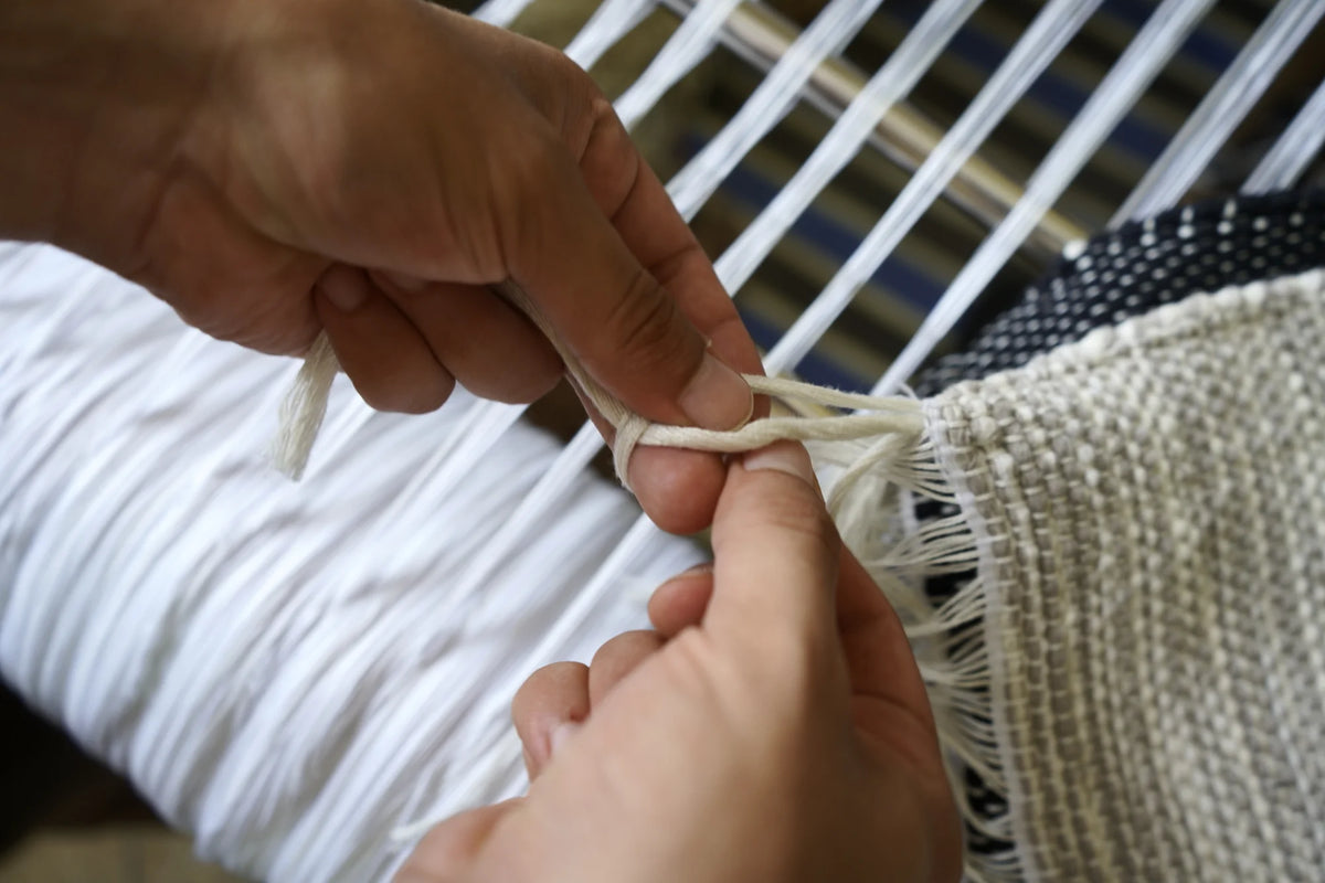 Mains d'artisane nouant les franges d'un tissage